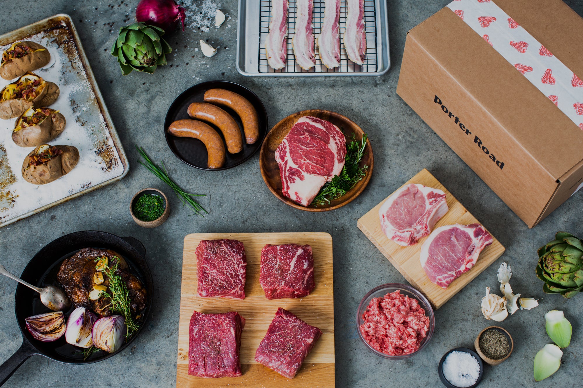 Denver steaks, sausage, ribeye steak, and pork chops on a table top with Porter Road delivery box