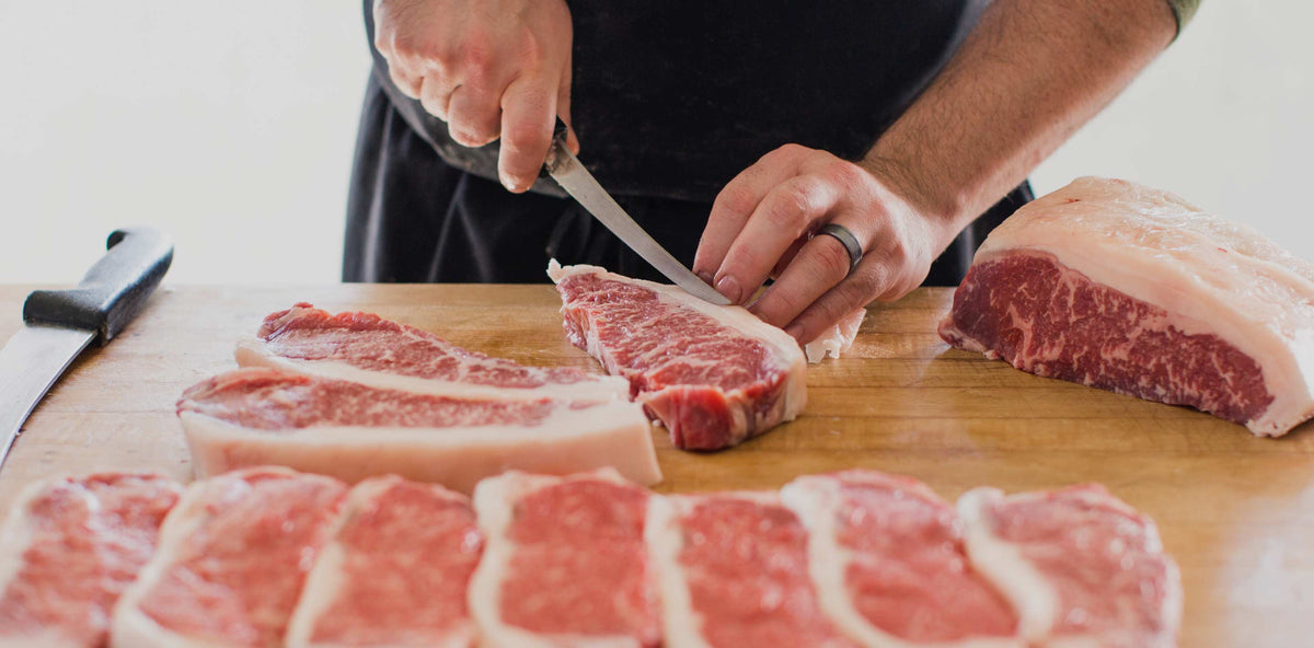 Butcher trimming dry-aged steaks on the butcher block